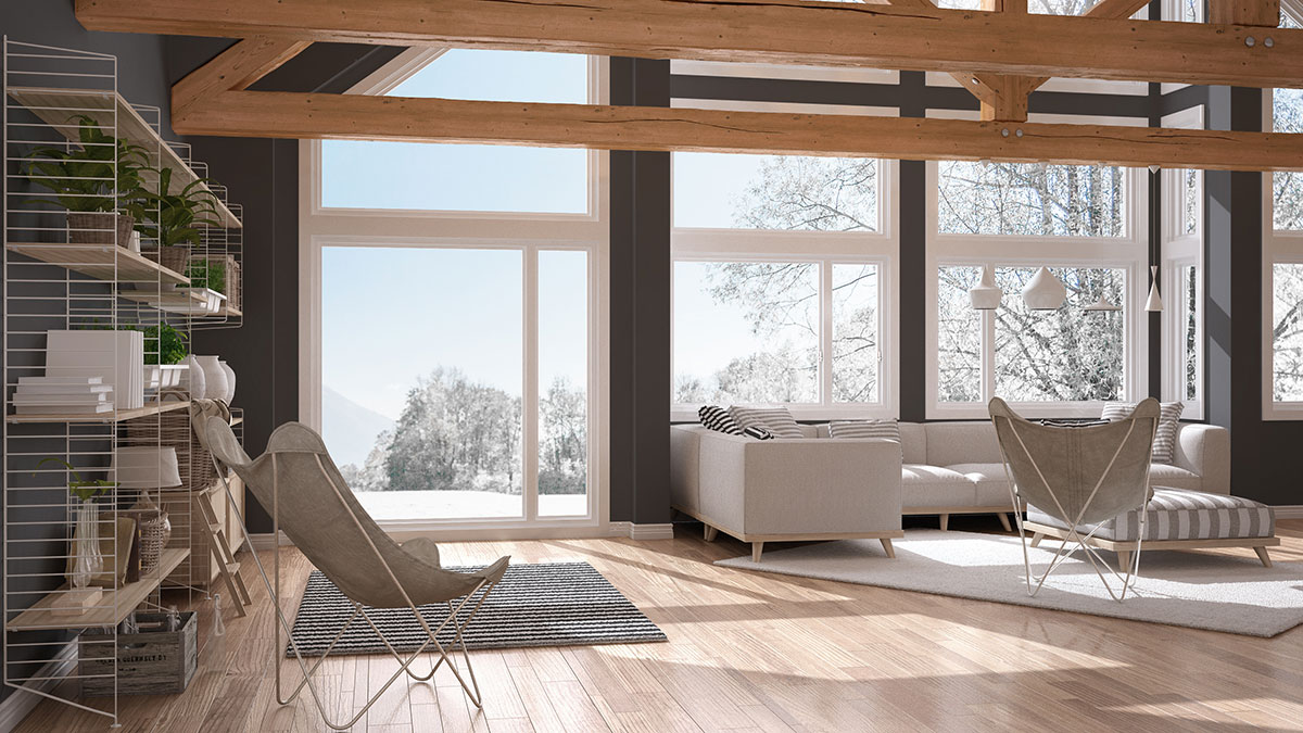 Grande soggiorno luminoso con divano chiaro, travi in legno a vista e pavimento parquet multistrato.
