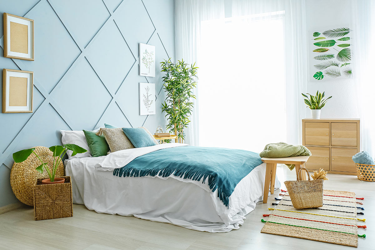 Camera da letto moderna con parete blu, mobili in legno chiaro e piante verdi.