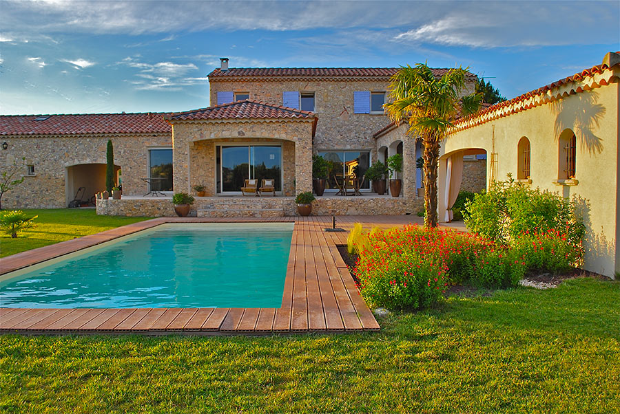 Grande casa in pietra con giardino e piscina rettangolare con bordi in legno.