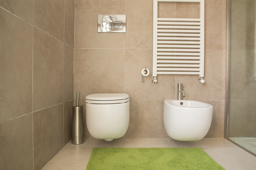 bagno moderno beige con sanitari sospesi bianchi e tappeto da bagno verde.