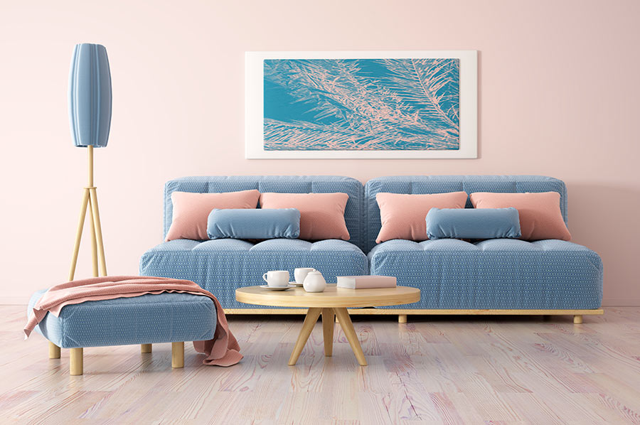 Soggiorno moderno minimal con parete rosa, divano blu pastello e tavolino tondo in legno chiaro.