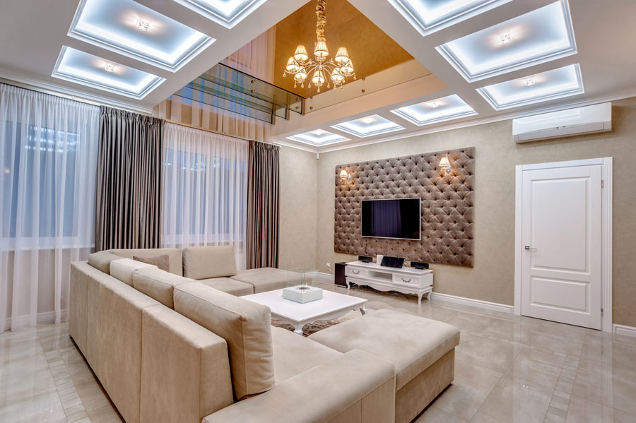 Salotto con divano angolare beige, pareti color tortora e parete TV color fango.