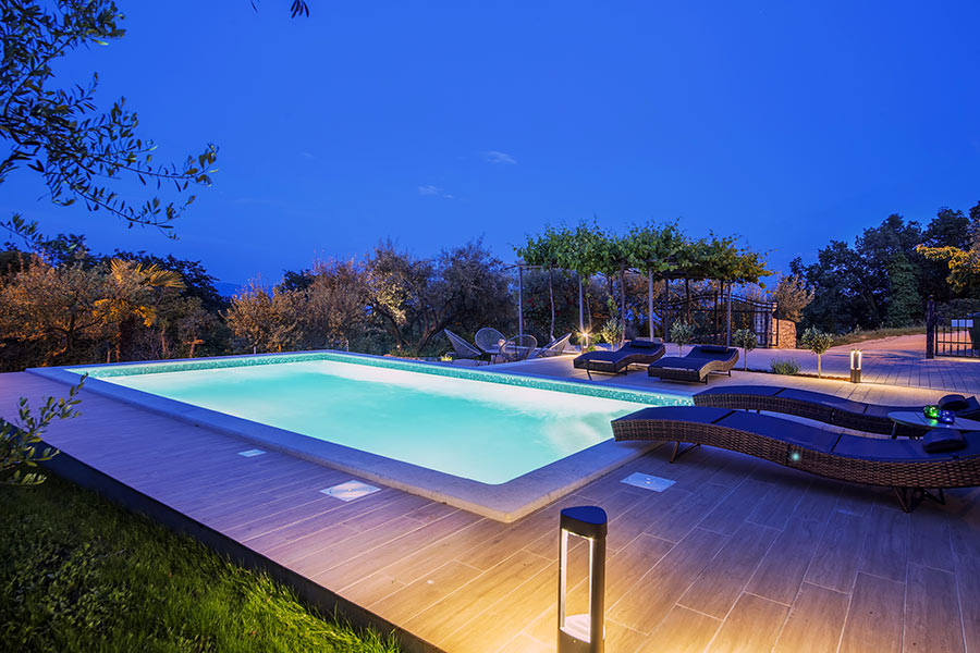 Bella piscina illuminata di sera con pavimentazione in legno.