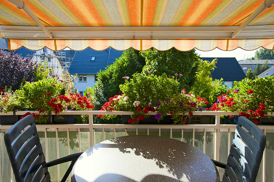 Vista di un balcone da l'interno con tende parasole e tavolo rotondo.