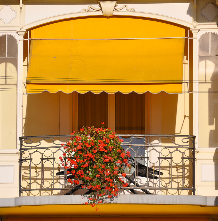 Balcone con tende da sole a caduto e fiori rosse.