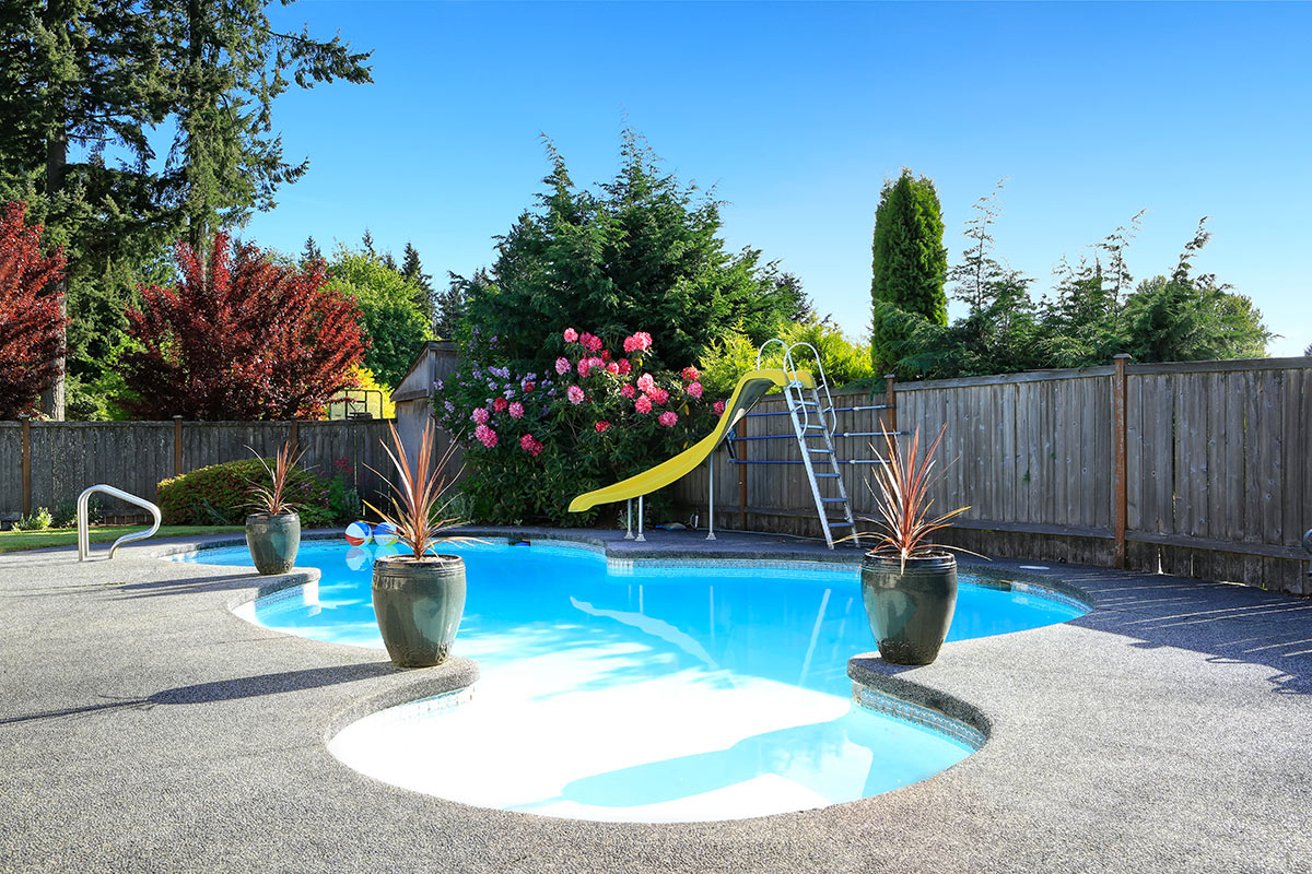 Bellissima piscina interrata a forma libera con scivolo, decorata con vasi di fiori.