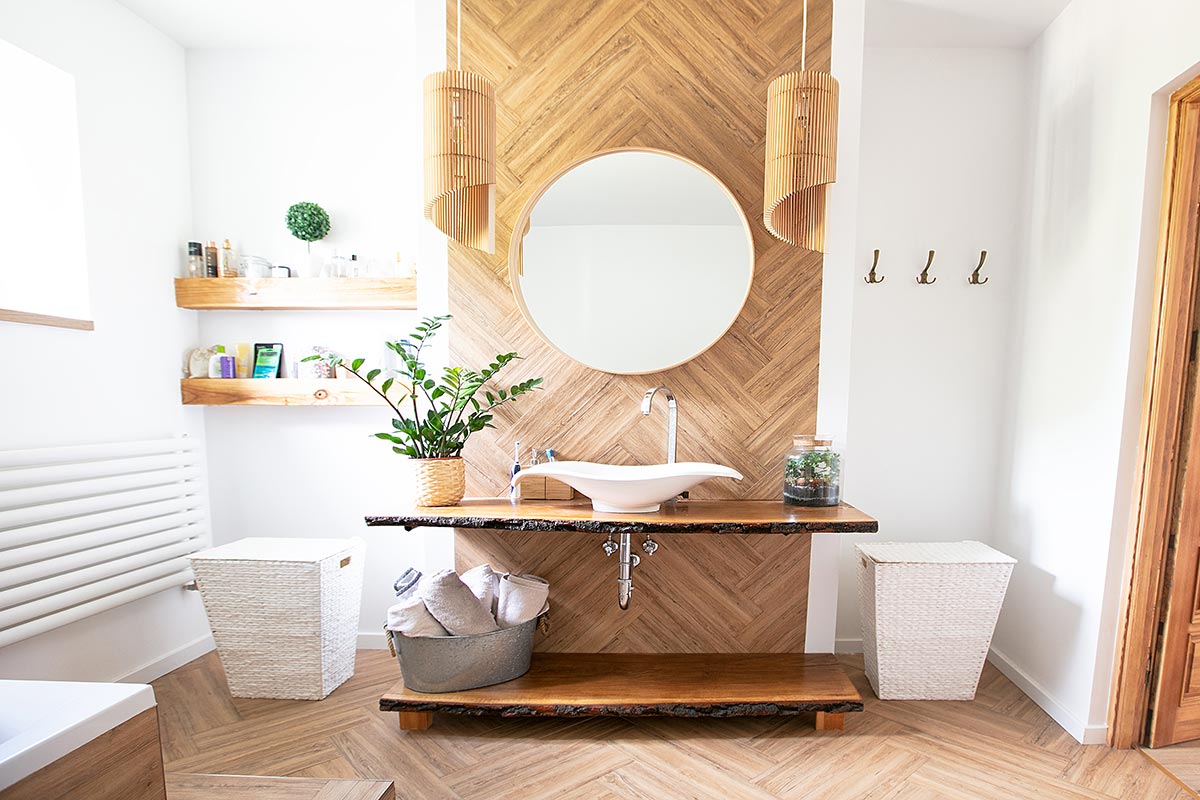 Bellissimo bagno in stile moderno con mobile lavabo in legno naturale, parete in legno e specchio rotondo.